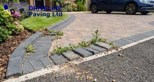 damaged driveway edging with loose border blocks, widened joints, and weeds growing along the edge